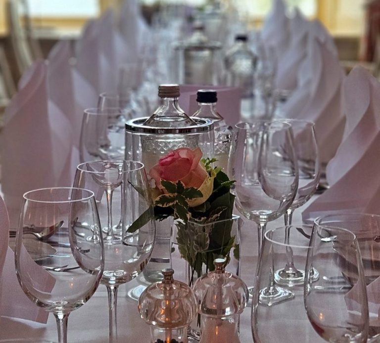 Elegant gedeckter Tisch mit Gläsern, einem Blumenarrangement und weißen Servietten.